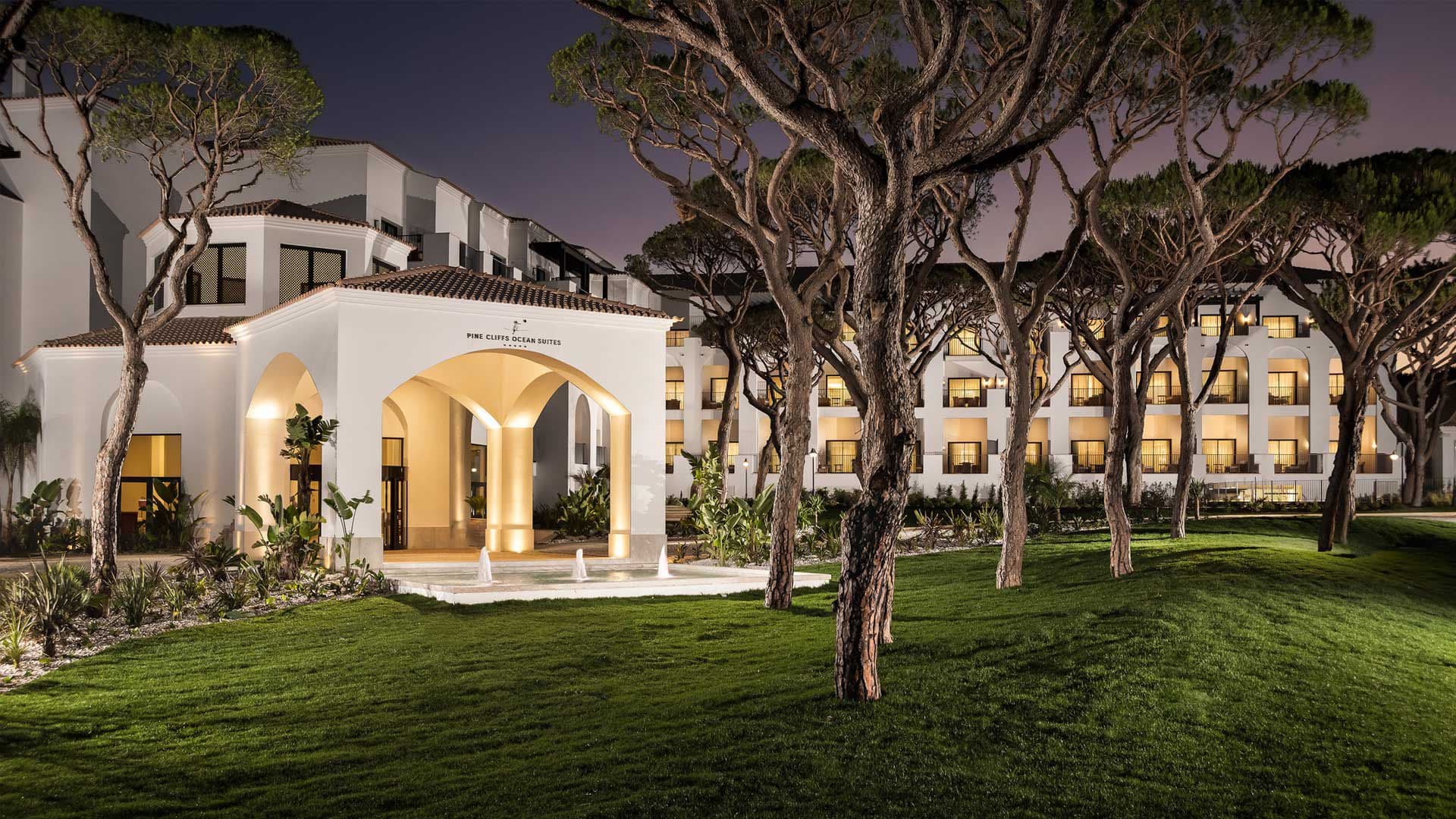 A UHM resort wing lit at dusk beneath the umbrella pines of the Algarve